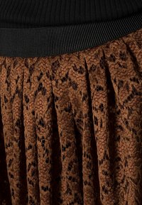 Bruine kantrok met een patroon en plooien, voorzien van een zwarte geribbelde tailleband. Bevat complexe uitsparingen in de stof.