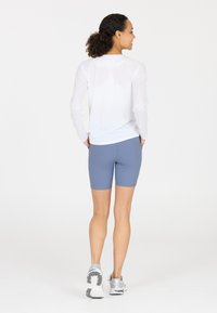 White long-sleeve athletic top paired with light blue shorts. Features a smooth texture, fitted design, and functional pockets. Gray sneakers.