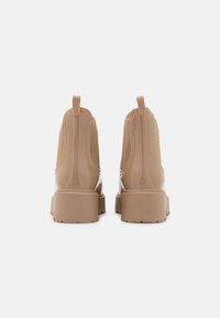 Botas de tobillo impermeables en color marrón con acabado suave, paneles laterales elásticos y lengüetas en la parte superior. Tacones gruesos y bloques con suelas texturizadas.