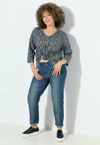 Modrý top s vzorem a zkrouceným předním dílem, tříčtvrteční rukávy, v kombinaci s světle modrými džíny a námořnickými teniskami. Hladká tkanina, volný střih.