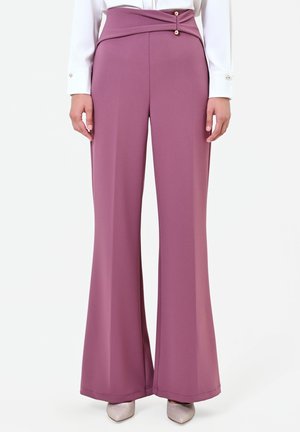 Pantalon large taille haute mauve avec une ceinture unique à chevauchement maintenue par deux boutons, porté avec un chemisier blanc à manches longues et des chaussures pointues.