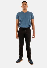 Blauw T-shirt met V-hals, zwarte broek met trekkoord en blauwe sneakers met bruine accenten. De stof lijkt zacht en de pasvorm casual.