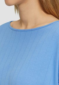 Helles blaues, geripptes Oberteil mit weitem, abgerundetem Ausschnitt, das dezente vertikale Linien und eine weiche Textur aufweist.