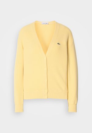 Cardigan giallo a maglia con scollo a V, chiusura con bottoni e polsini a costine. Presenta un piccolo logo verde sul lato sinistro del petto. Tessuto morbido.