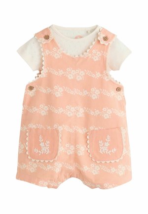 Peach floral short overalls with scalloped edges and wooden buttons over a white short-sleeve top with subtle eyelet pattern.