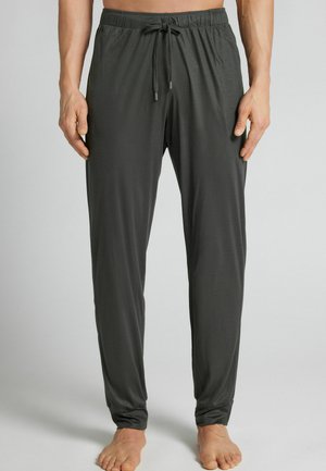 Pantalon ample gris foncé avec taille élastique et cordon, porté pieds nus par une personne debout sur un fond clair.