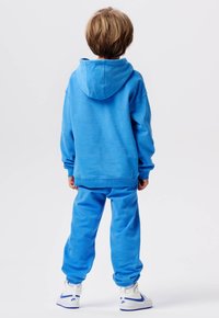 Blauwe hoodie en trainingsbroek set in zachte stof, met een pullover ontwerp met een capuchon en elastische mouwen, gecombineerd met witte sneakers.