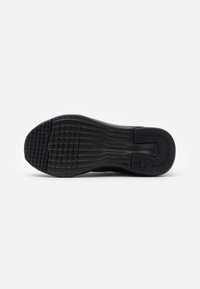 La suela de las zapatillas negras presenta una superficie de goma texturizada con ranuras para tracción, un diseño curvado y un detalle de logo.