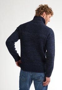 Pulover tricotat de culoare albastru marin, cu un guler înalt, având manșete și tiv cu textură nervurată, și o textură stropită pe întreaga țesătură.