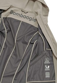 Waterdichte beige jas met grijze voering; bevat een gebrandmerkte "Bomboogie" print, meerdere opbergzakken en prestatie-iconen.