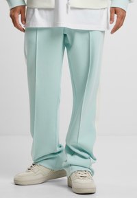 Helle blaue Jogginghosen mit seitlichen Falten und subtilen kontrastierenden cremefarbenen Streifen, hergestellt aus weichem Material und kombiniert mit beigen Sneakers.