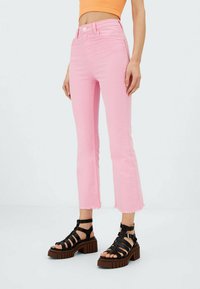 Rosa Jeans im Schlagstil mit rohem Saum und hoher Taille, kombiniert mit schwarzen, strappy Plattformsandalen mit einer klobigen Sohle.
