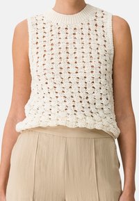 Top in maglia di un bianco cremoso con un design a trama larga e aperta, scollatura a coste e vestibilità rilassata, abbinato a pantaloni leggeri beige.
