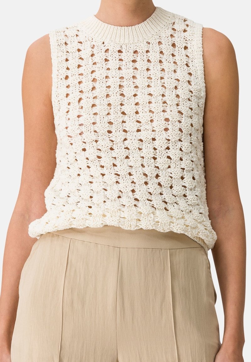 Top in maglia di un bianco cremoso con un design a trama larga e aperta, scollatura a coste e vestibilità rilassata, abbinato a pantaloni leggeri beige.