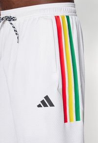 Calções atléticos brancos com um acabamento texturizado, apresentando cinco riscas verticais em vermelho, amarelo, verde e um logo da Adidas preto no canto inferior esquerdo.