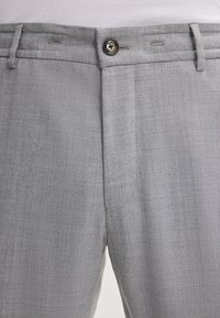 Pantaloni grigi realizzati in un tessuto testurizzato presentano una chiusura con bottone, passanti per cintura e dettagli di cucitura sottili. Design aderente con un aspetto sartoriale.