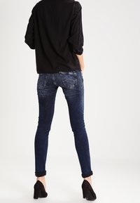 Jeans skinny blu scuro con una texture sbiadita e orli arrotolati, dotati di tasche posteriori con dettagli di cuciture sottili. Materiale: denim.