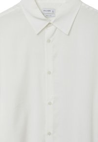 Camicia bianca con taglio squadrato, dotata di colletto classico, maniche lunghe e piccoli bottoni in stoffa lungo la parte anteriore. Tessuto liscio.