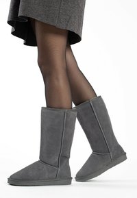 Botas altas de ante gris hasta la rodilla con punta redonda y detalle en las costuras laterales, que cuentan con una suela de goma texturizada y un forro de tela suave.