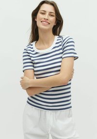 Camiseta de algodón a rayas con manga corta, con rayas horizontales en azul marino y blanco, y un cuello redondo blanco. El modelo lleva pantalones claros.