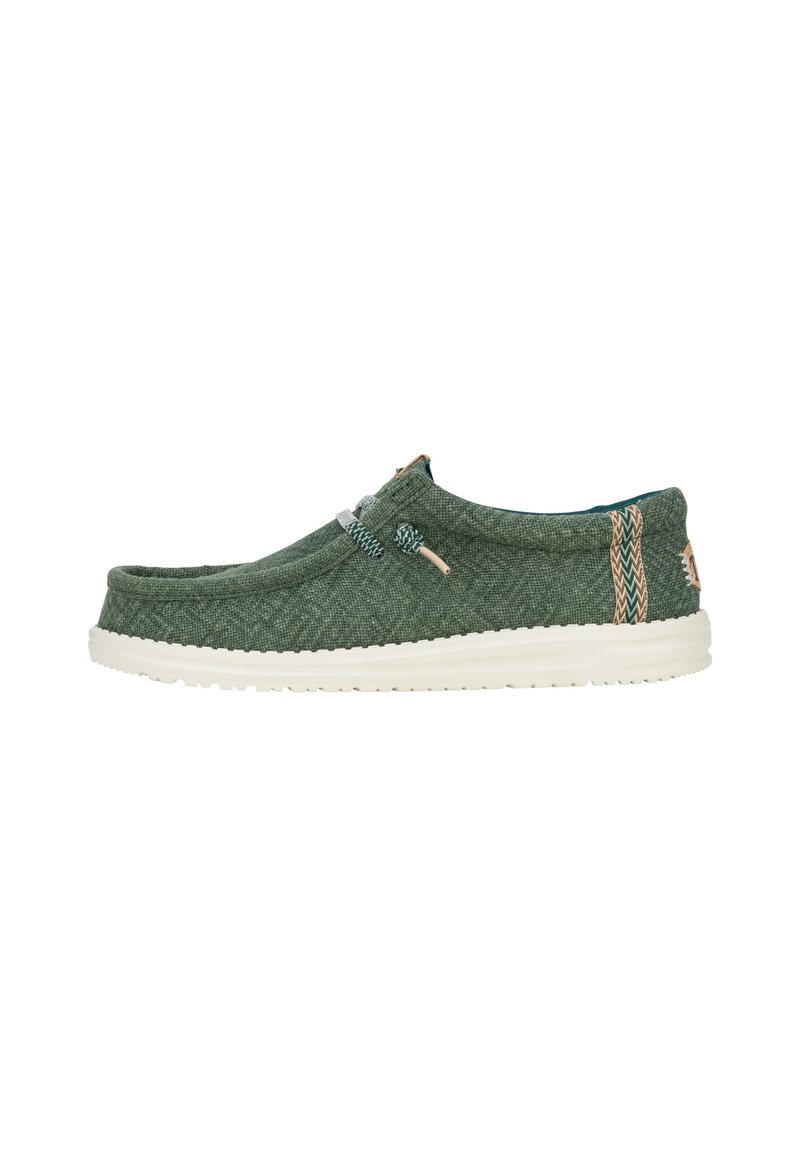 Scarpa slip-on in tessuto verde con suola in gomma bianca, dotata di lacci elastici e decorazioni con motivi sui lati. Superficie ruvida.