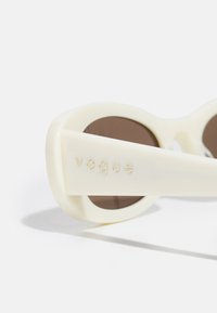 Valged plastikprillid pruunide läätsedega, julge ümara disainiga ja templel kuldsete tähtedega sõna "vogue".