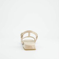 Sandal in pelle verniciata beige con tacco blocco basso, cinturino alla caviglia regolabile e dettaglio della fibbia circolare. Superficie liscia.