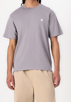 T-shirt gris en coton avec manches courtes et col rond. Présente un petit logo blanc sur la poitrine. Coupe ample, texture douce.