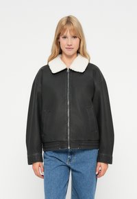 Μαύρο τεχνητό δερμάτινο μπουφάν με λευκό πλεκτό γιακά, μπροστινό φερμουάρ, πλαϊνές τσέπες και ribbed στρίφωμα; χαλαρή εφαρμογή με πτώση στους ώμους.