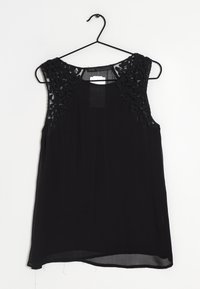 Zwarte mouwloze top met gestructureerde zwarte kantpanelen op de schouders, lichtgewicht stof en een iets gebogen zoom. Hangt aan een zwarte haak.