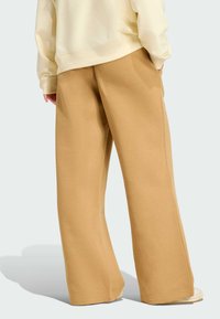 Pantalone širokog kroja od mekanog bež materijala, s glatkom teksturom, opuštenim fitom, bočnim džepovima i jednostavnim dizajnom donjeg ruba.
