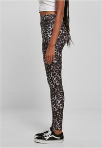 Leggings cu talie înaltă, într-un imprimeu animalier alb-negru, cu o textură netedă, asociate cu adidași negri cu accente albe.
