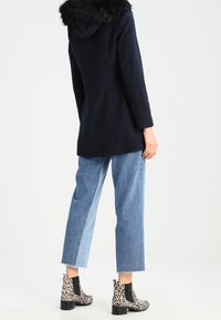 Navy coat with a faux fur hood, paired with cropped light blue jeans and black ankle boots featuring a leopard print design.