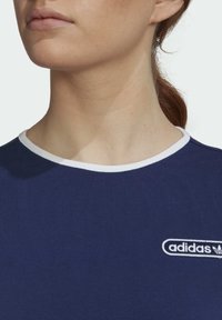 Mörkblå bomulls t-shirt med en vit ribbad rund halsringning, med en broderad Adidas-logotyp i vitt på bröstet.