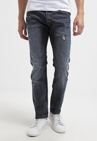 Mörkblå slitna jeans med hål, slim fit, med en blekt tvätt och subtila sömmar. Matchas med vita avslappnade sneakers.