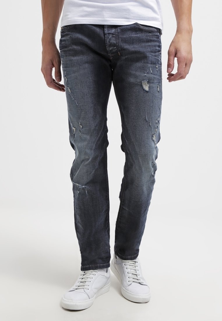 Mörkblå slitna jeans med hål, slim fit, med en blekt tvätt och subtila sömmar. Matchas med vita avslappnade sneakers.
