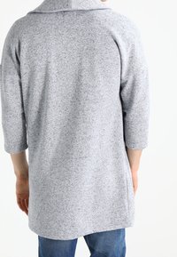 Gray, three-quarter sleeve, knit top featuring a high collar, a relaxed fit, and a soft, textured fabric. Back view shows its length.