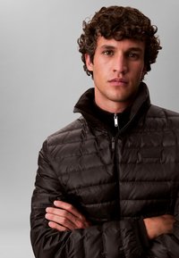 Must vuntsitud jope, krõmpsuv tekstuur, kõrge krae ja tõmblukuga kinnine. Sile kangas, kitsas lõige, rinnale on lisatud väike logo.