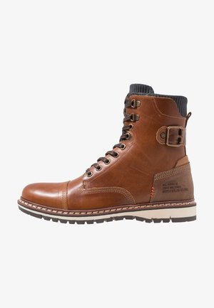 Braune Leder-Ankle-Boots mit strukturiertem Finish, Schnürsystem, geriffeltem Kragen, seitlichem Schnallenverschluss und kontrastierender weißer Gummisohle.