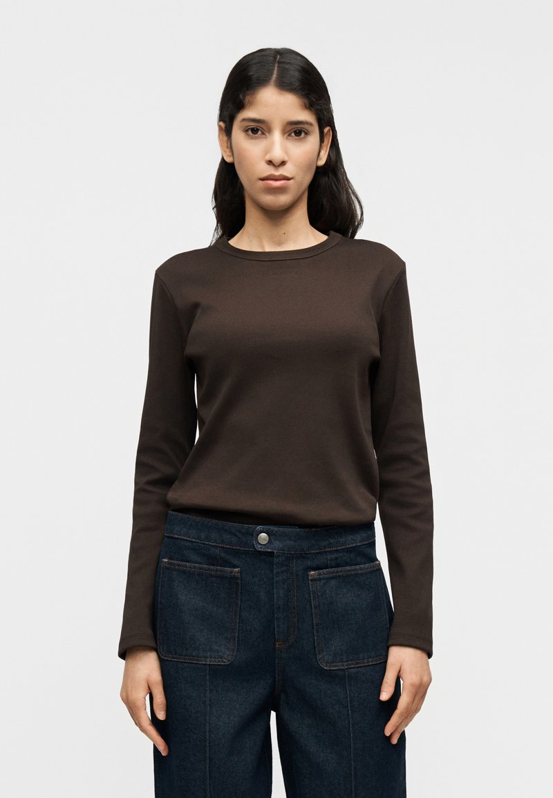 Καφέ μακρυμάνικο πουκάμισο από απαλό ύφασμα, με στρογγυλή λαιμόκοψη. Συνδυασμένο με σκούρο μπλε τζιν παντελόνι με μπροστινές τσέπες και εμφανή ραφές.