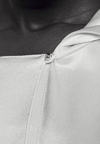 White satin top with a folded collar and small button closure. Smooth texture, subtle sheen, and minimalist design details.