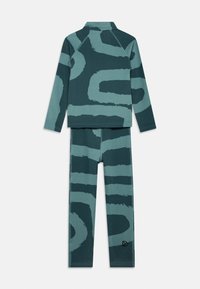Roheline ja teetooniline mustriga komplekt, mis sisaldab pika varrukaga toppi ja legginsid abstraktsete lainemustritega. Valmistatud tekstuuriga kangast, millel on nähtavad õmblused.
