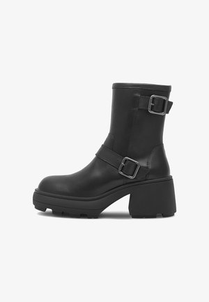 Juoda odinė kulkšnine batai su masyviu kulnu, turintis šoninę sagtį, apvalų nosį ir tekstūruotą padą geresnei sukibimui.