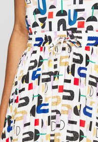 Robe à motifs multicolores avec taille élastique et cordon de serrage. Présente des formes géométriques audacieuses en noir, bleu, rouge et jaune sur un fond blanc.
