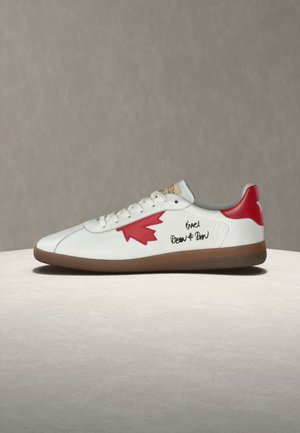 Zapatilla blanca de caña baja con diseño de hoja de arce roja, lengüeta del talón roja, suela marrón y texto negro estilo escrito a mano en el lateral.
