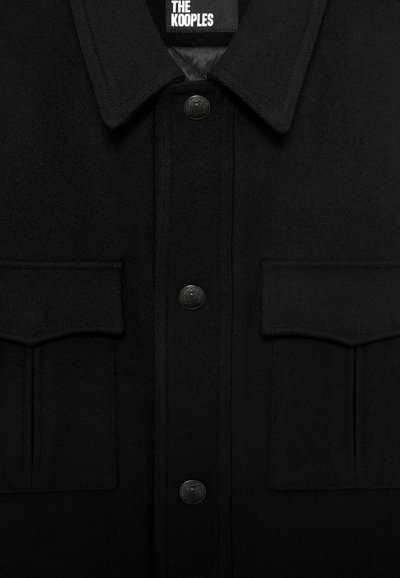 Giacca nera in lana con colletto, tre bottoni neri in rilievo e due tasche frontali a soffietto, etichettata "THE KOOPLES" all'interno del colletto.