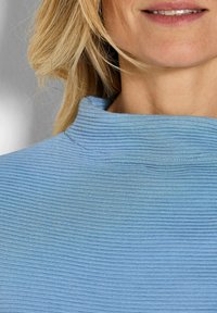 Lichtblauwe, geribbelde coltrui met een gestructureerde afwerking, voorzien van een hoge kraag en een strakke pasvorm rond de nek en schouders.