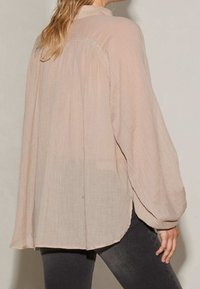 Blusa rosa chiaro a maniche lunghe realizzata in tessuto trasparente, con vestibilità comoda, schiena plissettata e orlo arrotondato, dotata di colletto alto.
