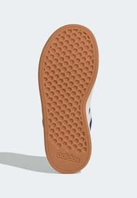 Semelle en caoutchouc d'une chaussure adidas, avec un motif de semelle hexagonal, de couleur marron clair, et un logo embossé près du talon.