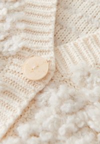Dicker Strickcardigan in Creme mit strukturierten Bobbel-Details. Verfügt über einen großen, marmorierten runden Knopf an einem gerippten Rand.
